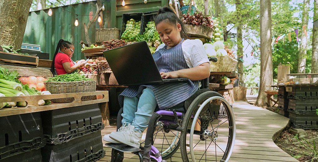 Persoana cu acondroplazie lucreaza pe laptop in scaun rulant